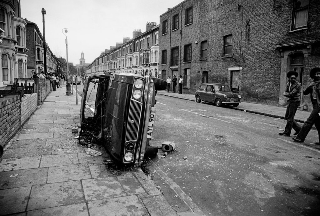 A burnt out car lies on its side in Railton Rd
