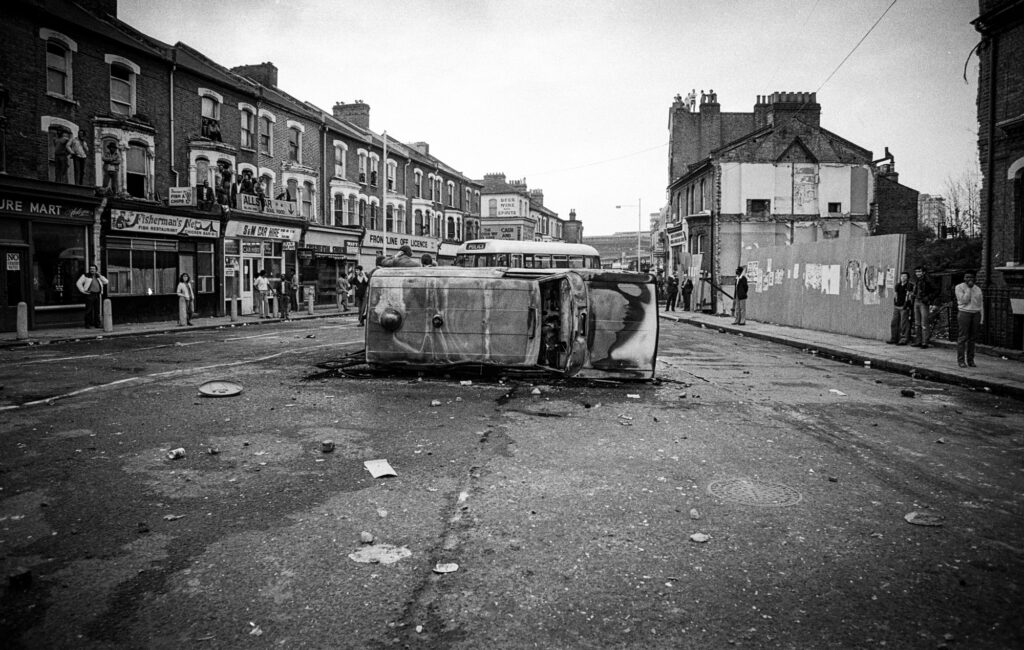 Coldhabour Lane; more burnt police vehicles. Again, residents remain in the area watching events unfold.